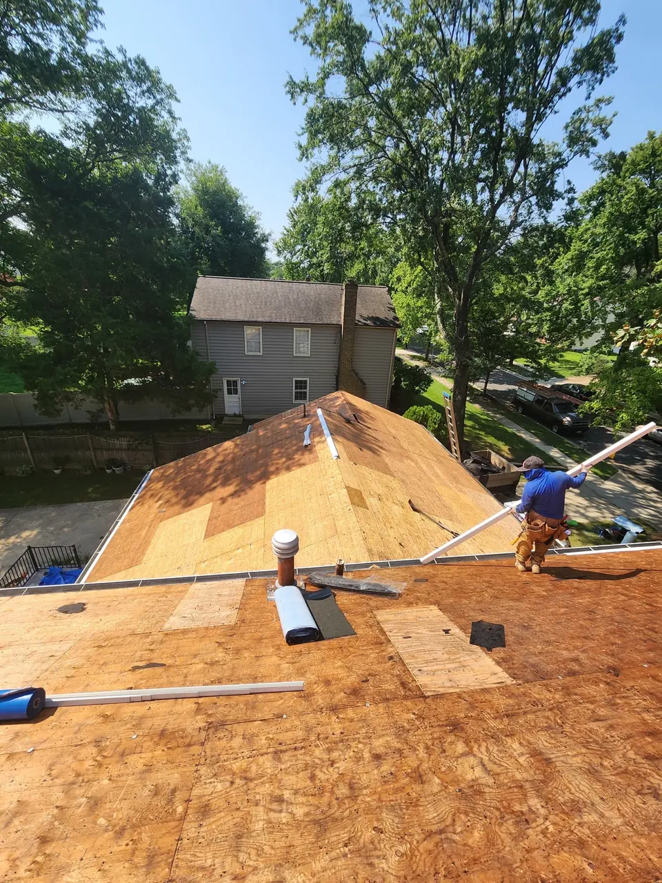 Installer handling a long edge component above exposed plywood roofing and pipe penetrations