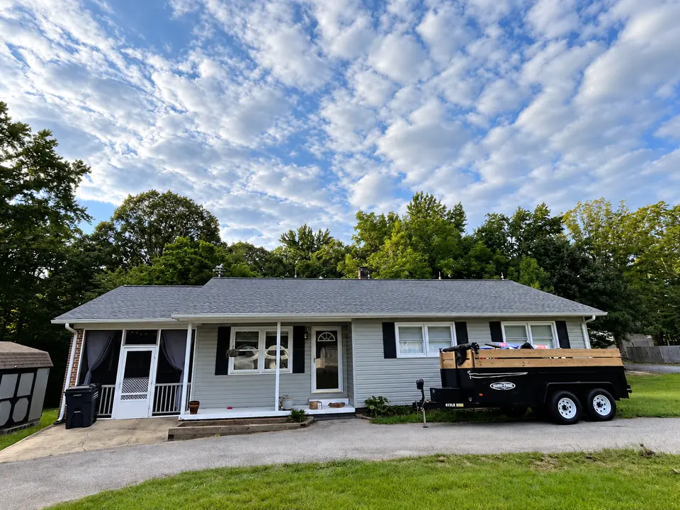 Single-story home with gray shingle roofing and a debris trailer in the driveway