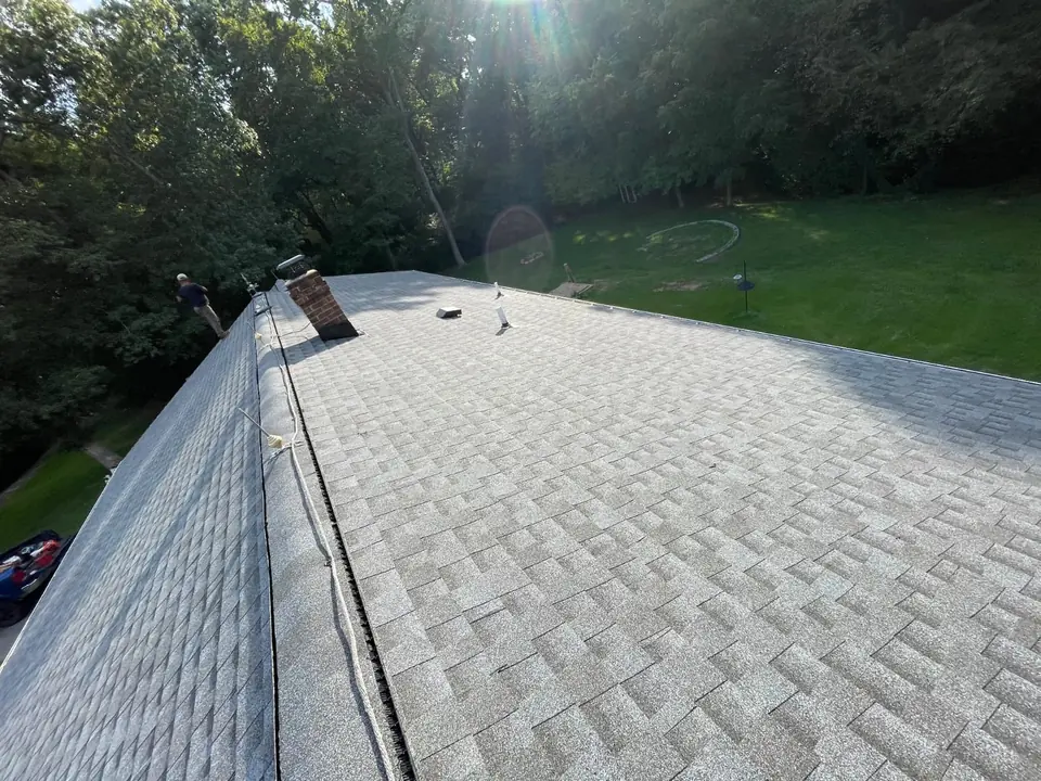 Gray asphalt shingle courses beside a brick chimney, roof vents and ridge