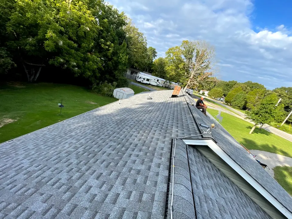 Gray architectural shingles around an intersecting roof section, with an installer near the ridge